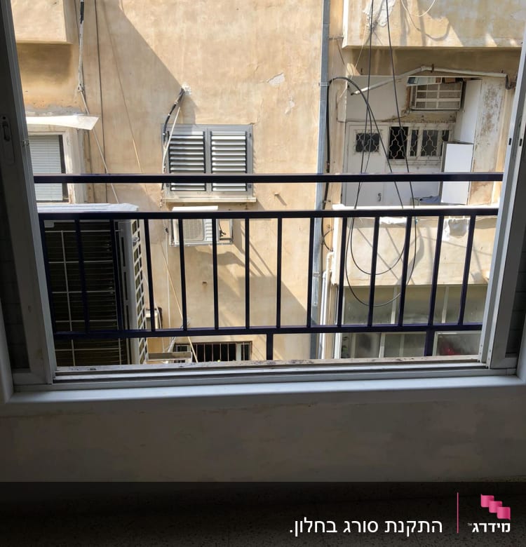 מסגרת חלון עם סורגי מתכת מול בניין סמוך